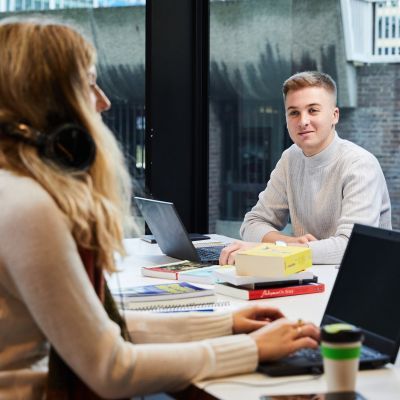 Man and woman on opposite sides of desk with laptops and books